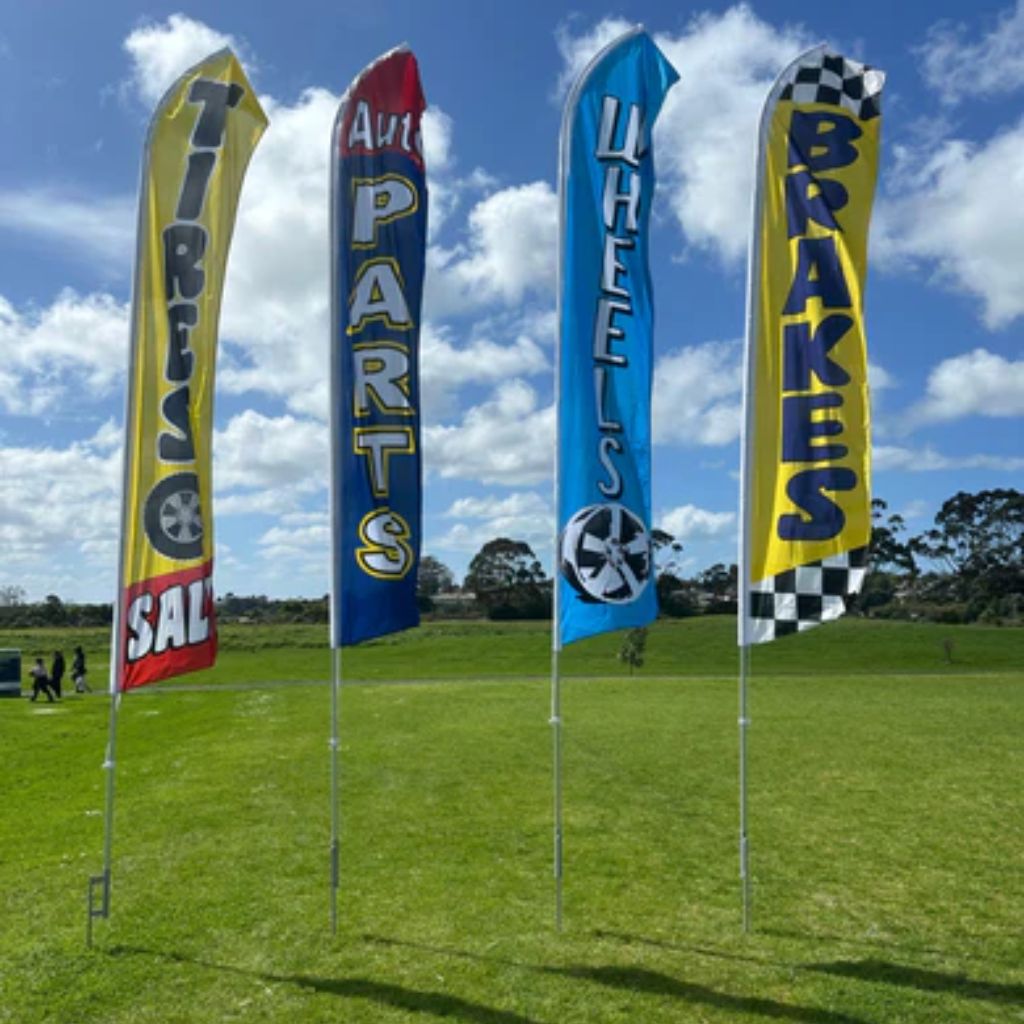 Four promotional flags for automotive parts on a grassy field with a blue sky.